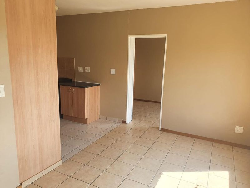An open-plan living and kitchen area featuring neutral wall tones, tiled flooring, and compact built-in kitchen cabinetry.
