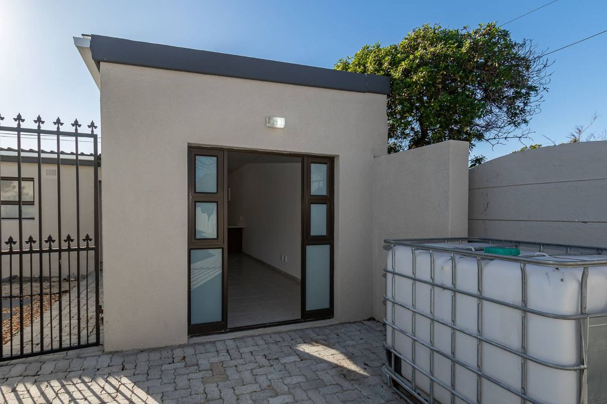 A view of the rear exterior area featuring a paved courtyard, secure wrought iron gate, and a modern entrance door to the property.