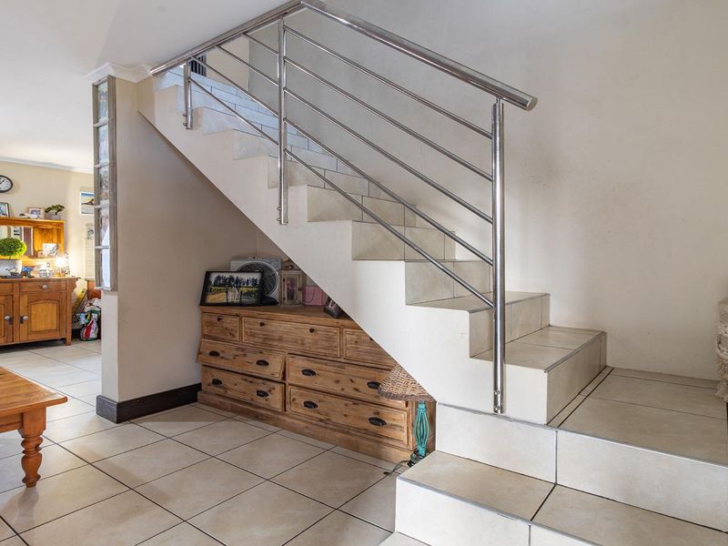 A tiled staircase featuring a modern stainless steel balustrade, situated in an open-plan living area with neutral ceramic floor tiles.