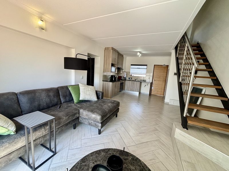 Open-plan living area featuring herringbone tile flooring, a modern kitchen with built-in cabinetry, and a staircase with a contemporary metal railing.