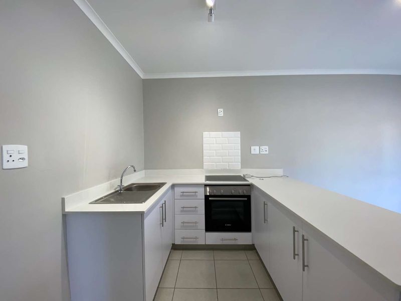 A clean, modern kitchen featuring white cabinetry, quartz countertops, a subway tile backsplash, and integrated oven and hob.