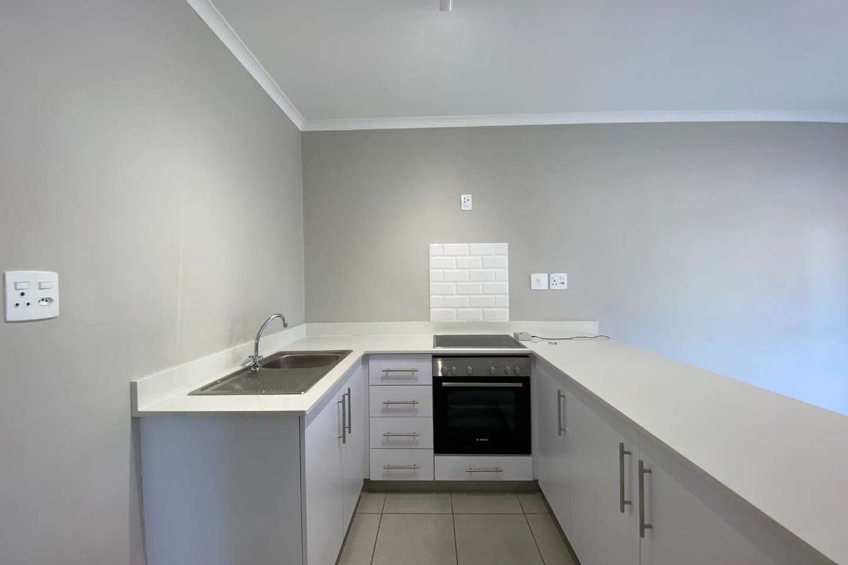 A clean, modern kitchen featuring white cabinetry, quartz countertops, a subway tile backsplash, and integrated oven and hob.