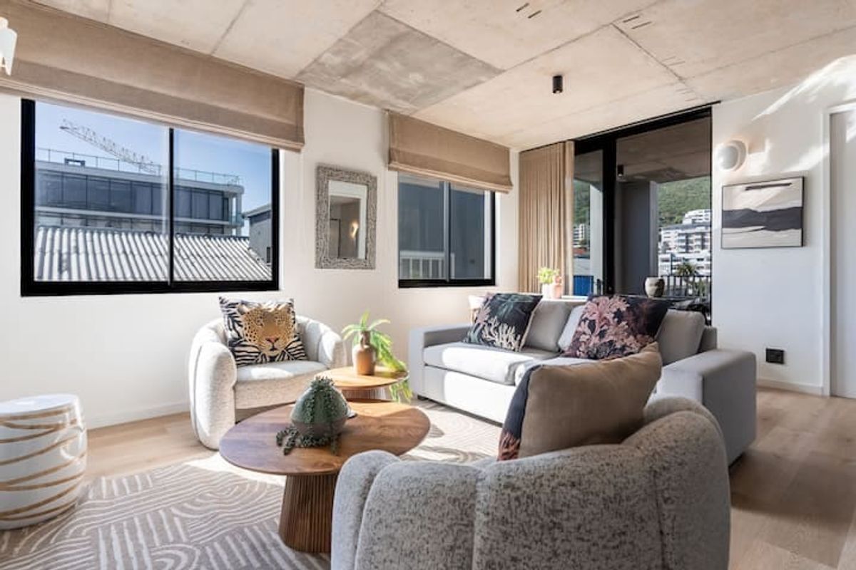 Modern living room featuring an exposed concrete ceiling, light hardwood flooring, and large windows providing ample natural light and access to a balcony.