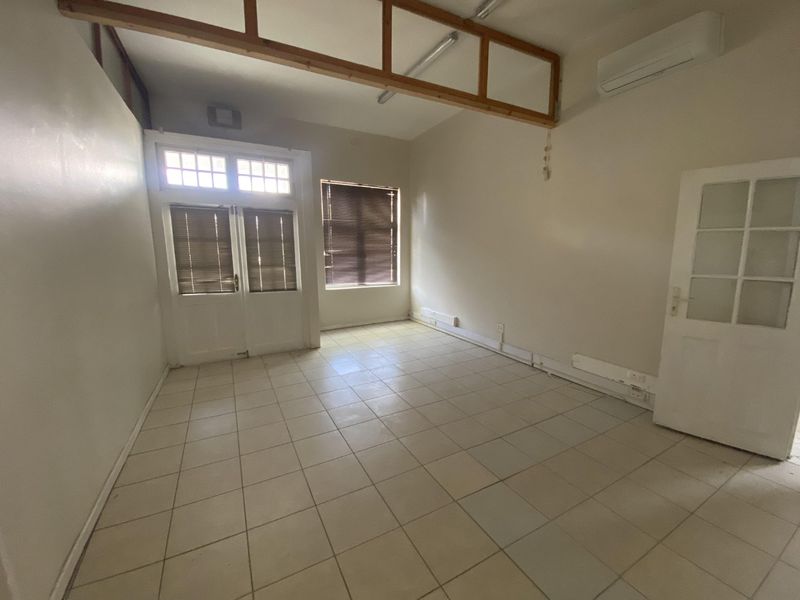 An empty office space featuring tiled flooring, a split-system air conditioner, and natural light through multi-pane glass doors and windows.