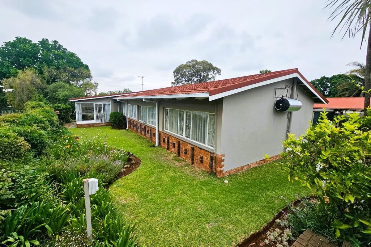 Rear view of the house featuring a tiled roof, brick accents, large windows, and a well-maintained garden with established landscaping.