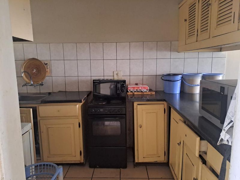 A functional kitchen featuring dated yellow cabinetry, tiled backsplash, dark countertops, and a freestanding stove, offering potential for a modern renovation.