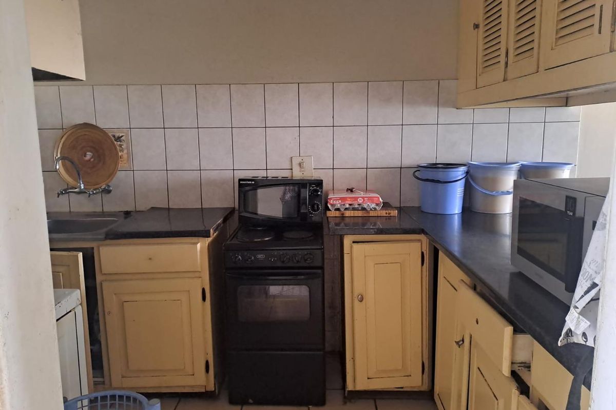 A functional kitchen featuring dated yellow cabinetry, tiled backsplash, dark countertops, and a freestanding stove, offering potential for a modern renovation.