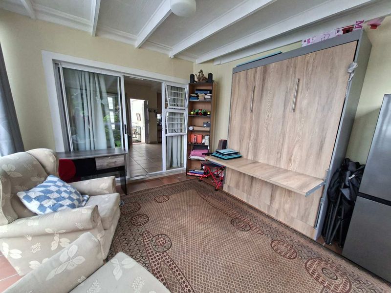 A living area featuring exposed ceiling beams, tiled flooring, and sliding glass doors leading to an adjacent space, equipped with a built-in wall bed.