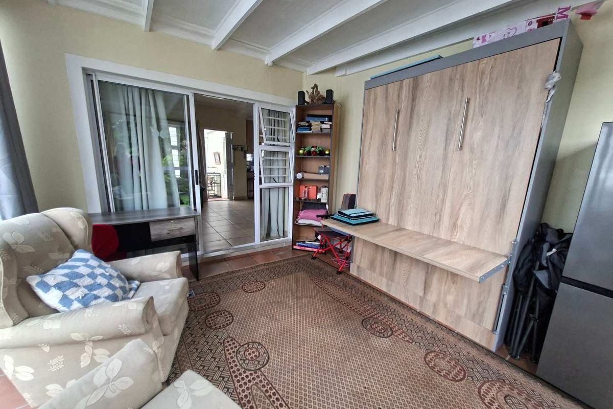 A living area featuring exposed ceiling beams, tiled flooring, and sliding glass doors leading to an adjacent space, equipped with a built-in wall bed.