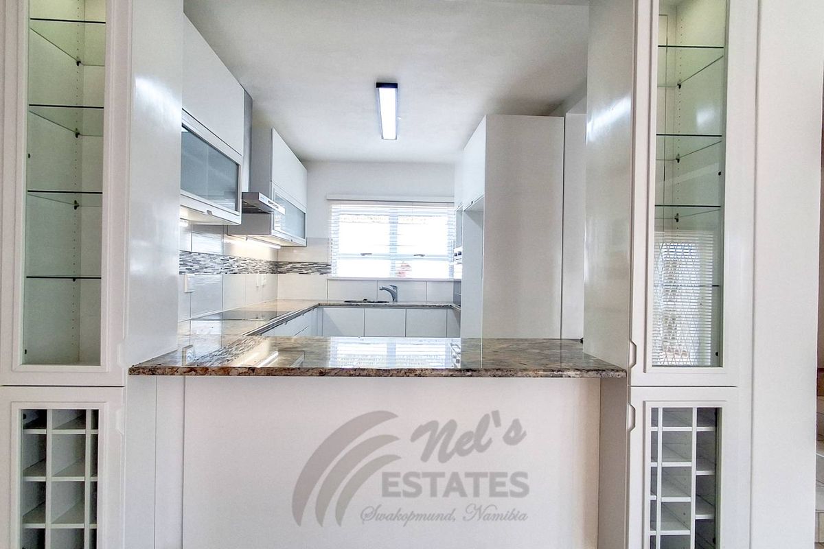 Modern kitchen featuring white cabinetry, granite countertops, a breakfast bar, and built-in glass display shelving.