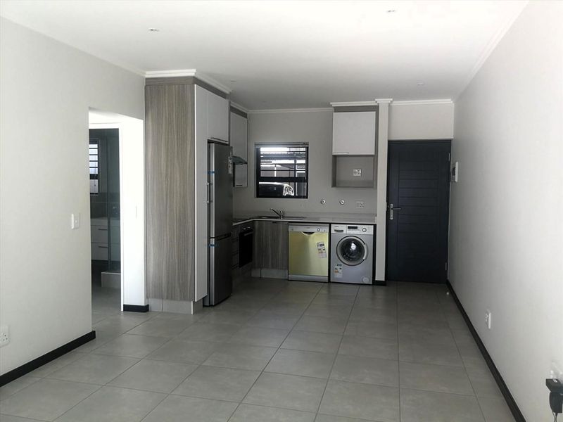 Modern open-plan kitchen featuring sleek built-in cabinetry, tiled flooring, and integrated appliance spaces, offering a clean and functional living area.