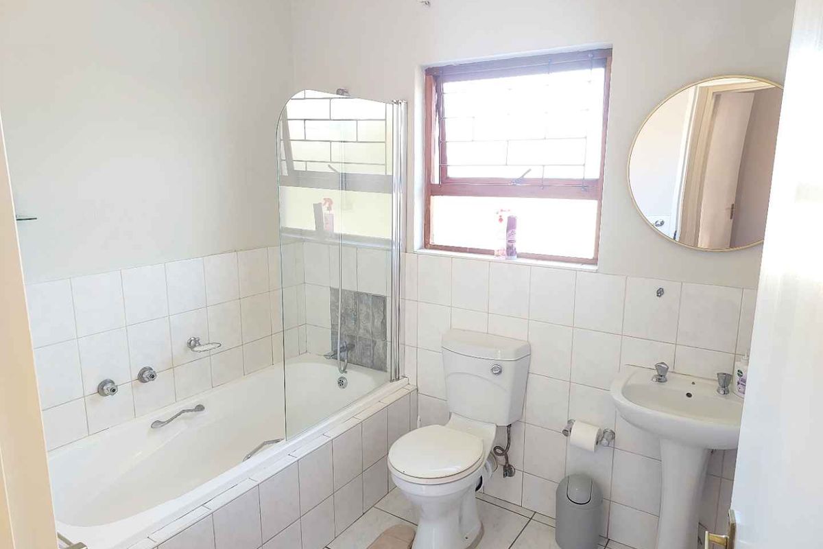 A functional bathroom featuring a bathtub with a glass screen, pedestal basin, and toilet, finished with neutral wall and floor tiles.