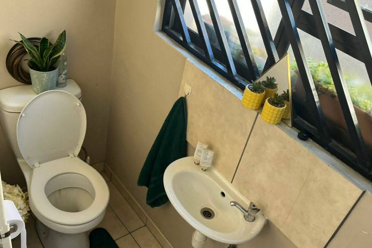 A compact guest bathroom featuring a wall-mounted basin, a standard toilet, and a security-grilled window providing natural light.