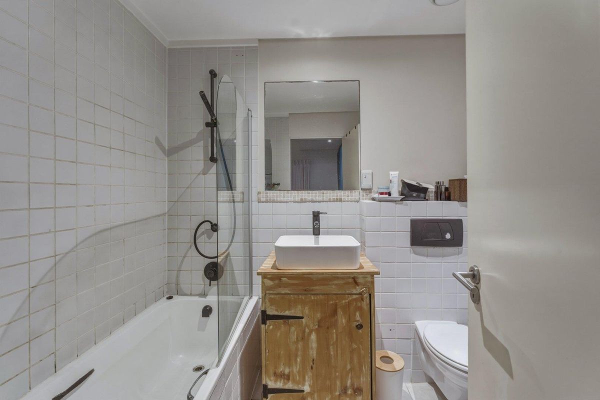 Compact bathroom featuring a bathtub with glass screen, vessel sink on a rustic vanity, and a wall-mounted toilet with concealed cistern.