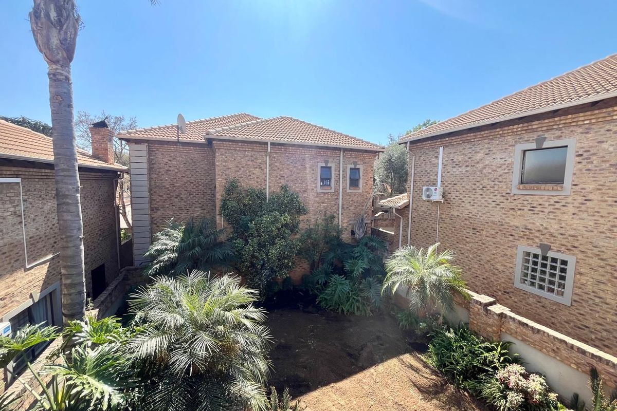 Rear view of the townhouse complex featuring face brick architecture, tiled roofing, and a private garden area with established greenery.