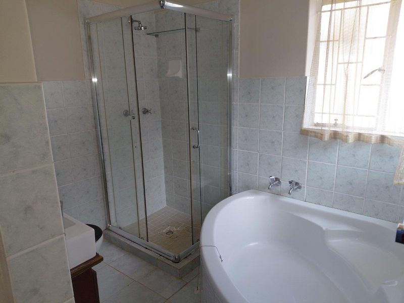A functional bathroom featuring a glass shower enclosure, a built-in bathtub, and tiled finishes throughout.
