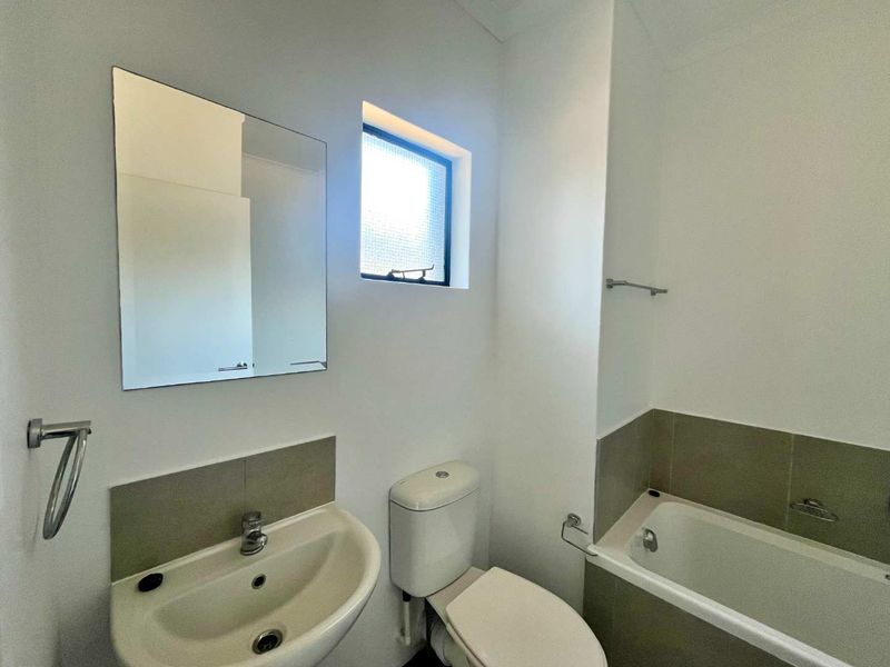 A clean and functional bathroom featuring a pedestal basin, toilet, and bathtub with neutral tiled splashbacks and a wall-mounted mirror.