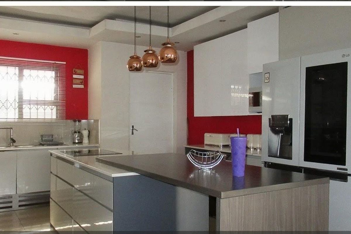 Modern kitchen featuring a central island, sleek cabinetry, built-in appliances, and contemporary pendant lighting with a bold red accent wall.
