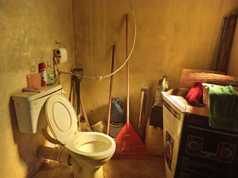 A small, utilitarian bathroom space featuring a standard toilet and exposed plumbing, currently in need of significant maintenance and cosmetic renovation.