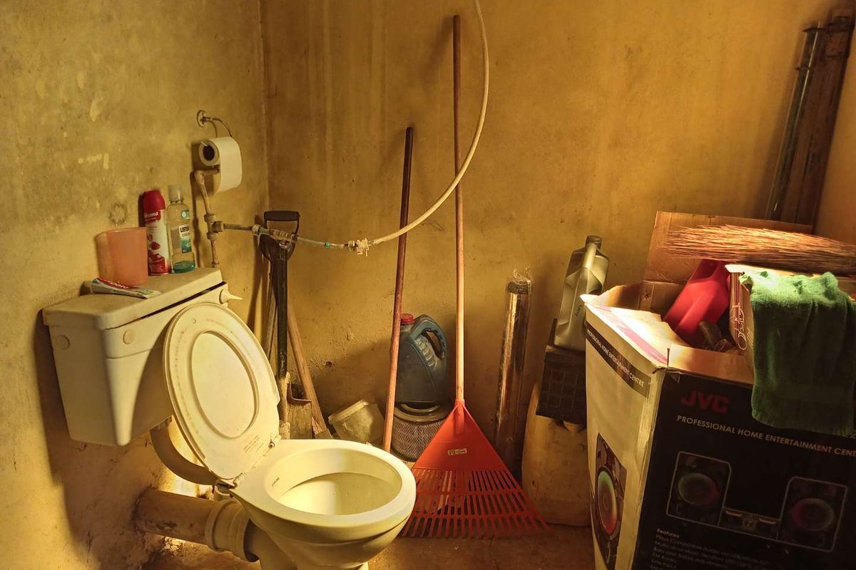 A small, utilitarian bathroom space featuring a standard toilet and exposed plumbing, currently in need of significant maintenance and cosmetic renovation.