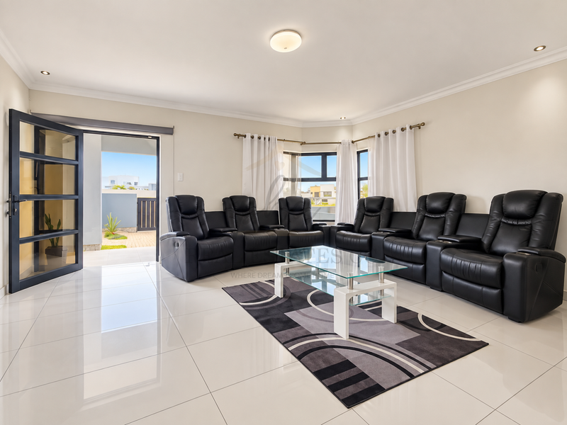 Spacious living room featuring polished porcelain tile flooring, recessed lighting, and large aluminium-framed windows providing access to an outdoor patio area.