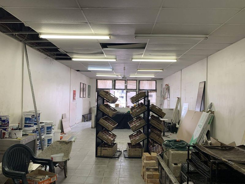 Open plan retail space featuring tiled flooring and suspended ceiling with fluorescent lighting, currently requiring maintenance and ceiling repairs.