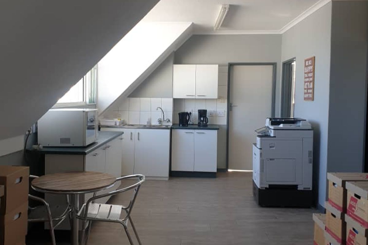 A functional kitchenette area featuring white cabinetry, a stainless steel sink, and tiled splashback, situated within an open-plan office space.