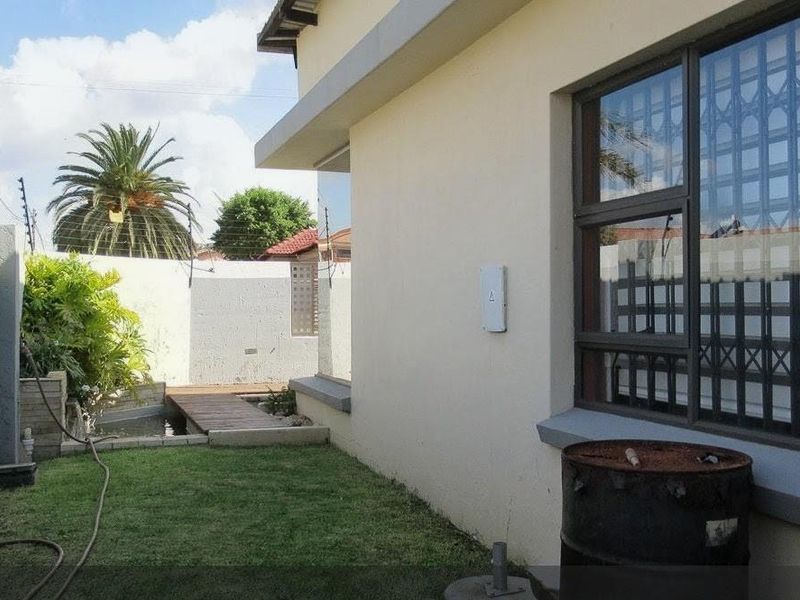 Rear exterior view showing a small garden area, boundary wall with electric fencing, and a small water feature with a wooden deck.