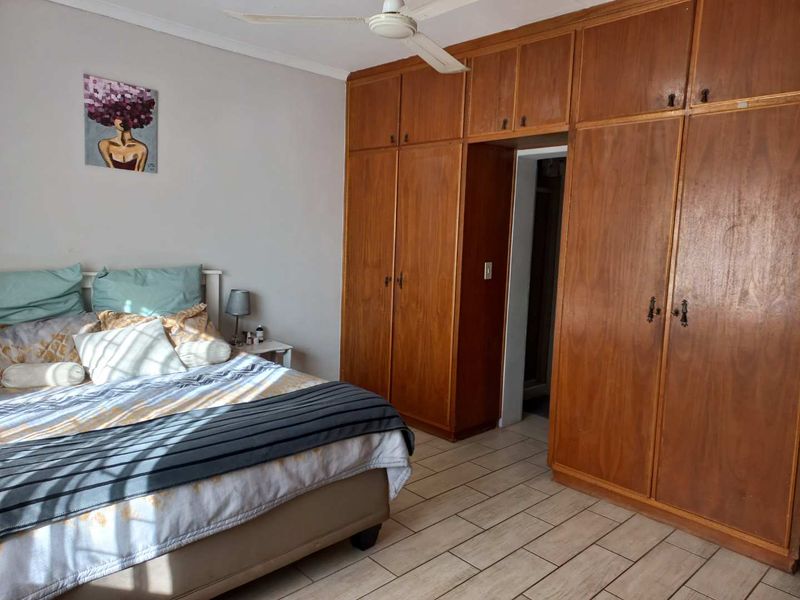 A bedroom featuring extensive built-in wooden cabinetry, tiled flooring, and a ceiling fan, offering functional storage and a neutral layout.