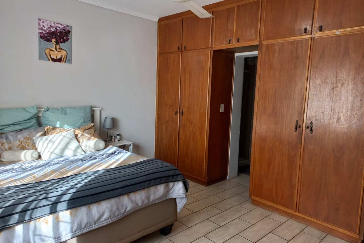 A bedroom featuring extensive built-in wooden cabinetry, tiled flooring, and a ceiling fan, offering functional storage and a neutral layout.