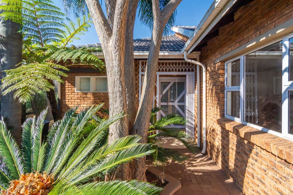 A well-maintained face brick front entrance featuring a paved walkway, secure gate, and established garden surroundings.