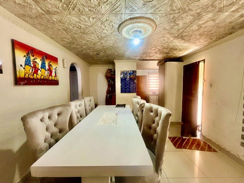 Dining room featuring decorative ceiling tiles, a central ceiling rose, and tiled flooring, leading to an adjacent living area through an archway.