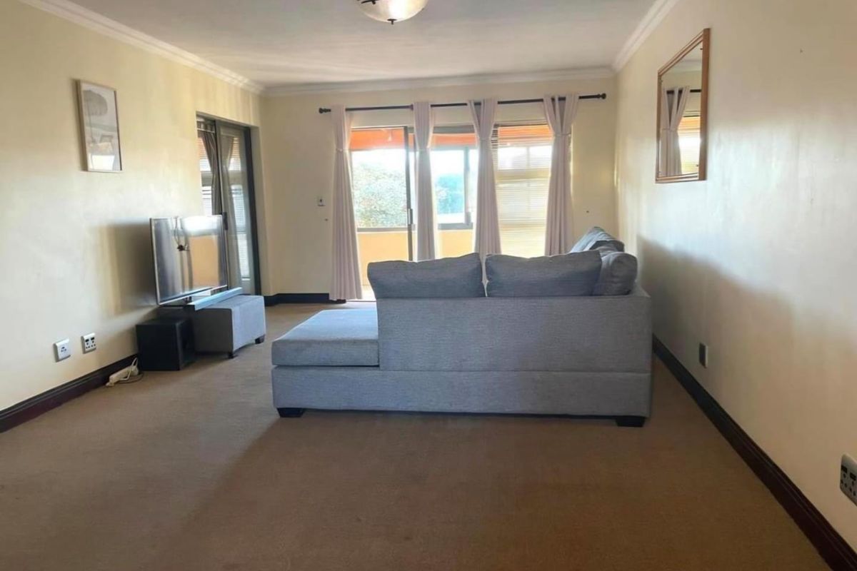 A spacious living room featuring carpet flooring, cove molding, and large sliding glass doors that provide access to an outdoor balcony area.