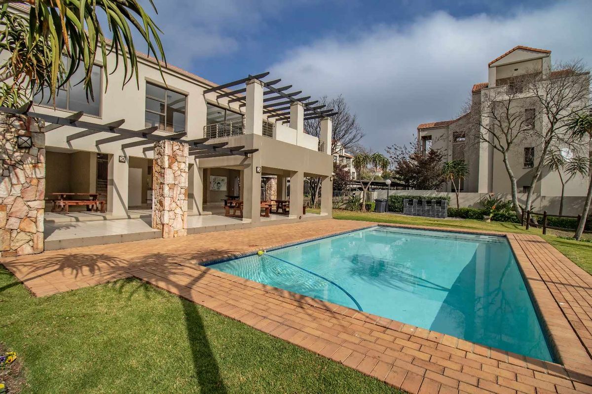A spacious rear exterior view featuring a swimming pool, paved surround, and a covered patio area with timber pergola structures.