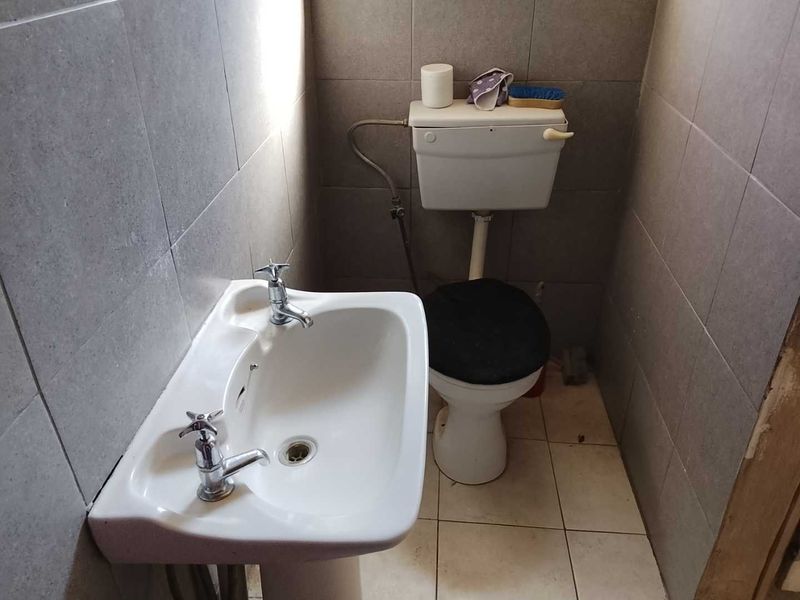 A compact bathroom featuring a pedestal basin and standard toilet with full-height ceramic wall tiling.