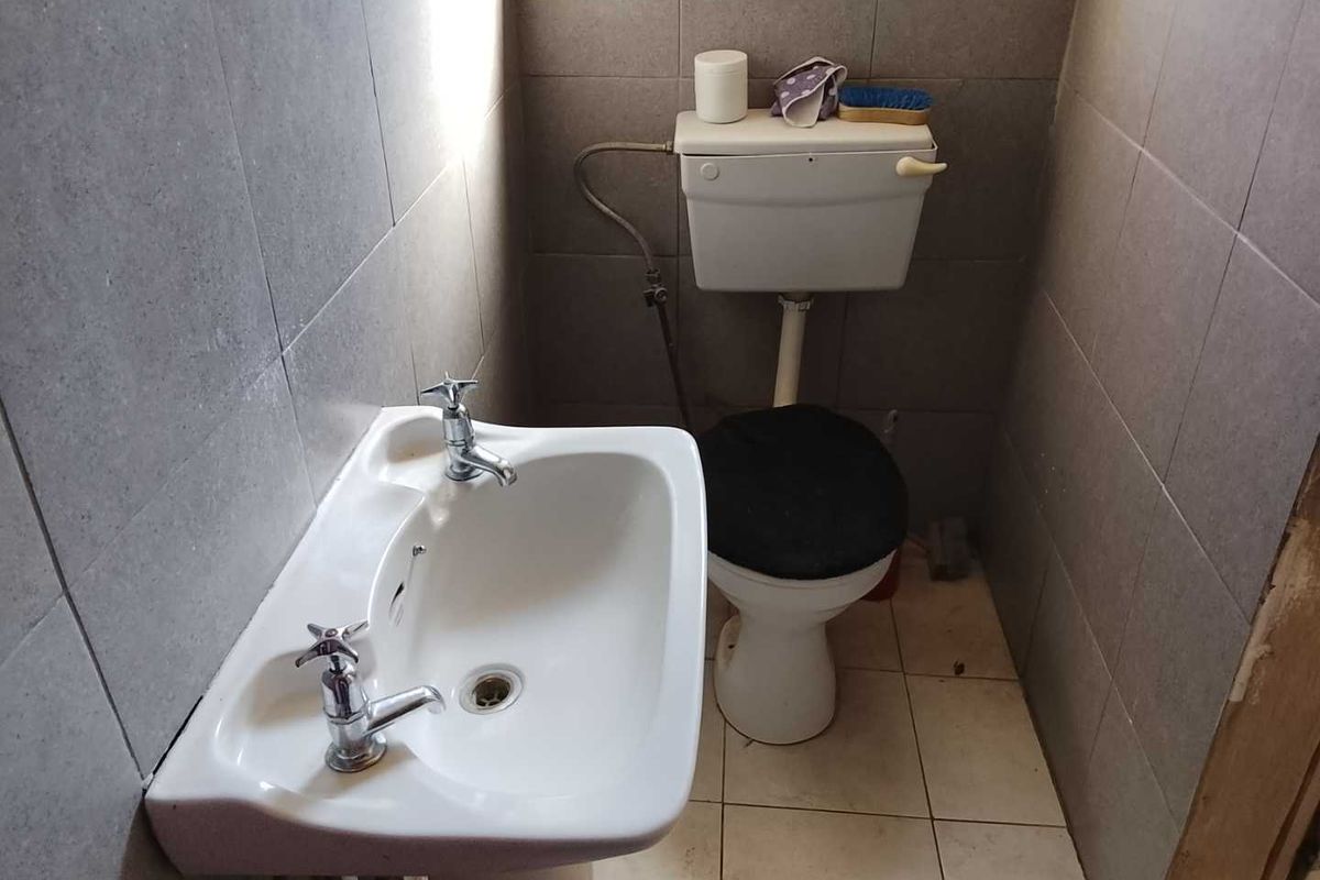 A compact bathroom featuring a pedestal basin and standard toilet with full-height ceramic wall tiling.