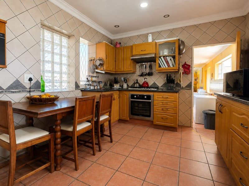 A functional kitchen featuring wooden cabinetry, integrated oven and hob, tiled backsplash, and a dedicated dining area with terracotta floor tiles.