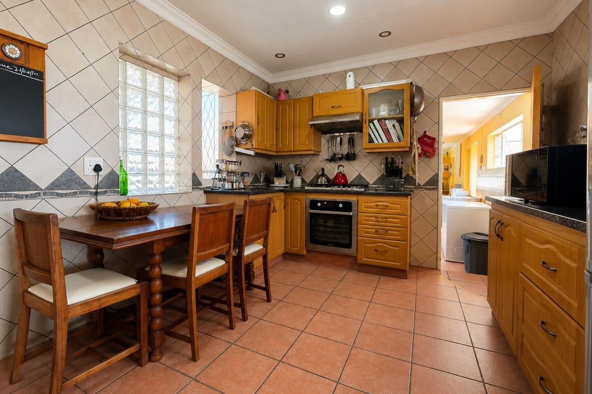 A functional kitchen featuring wooden cabinetry, integrated oven and hob, tiled backsplash, and a dedicated dining area with terracotta floor tiles.