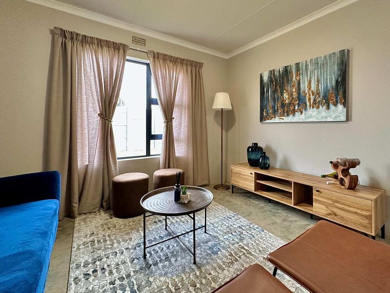 A well-maintained living room featuring neutral wall tones, coved ceilings, and a large window providing natural light.