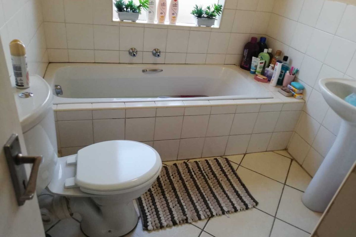 A functional bathroom featuring a built-in bathtub, pedestal sink, and toilet with tiled walls and flooring.