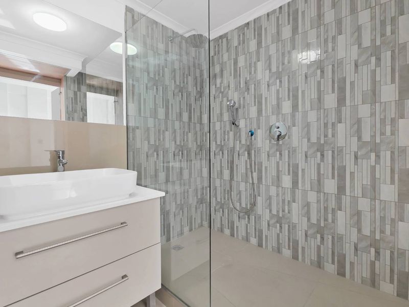 Modern bathroom featuring a sleek vanity with vessel sink, large wall mirror, and a spacious walk-in shower with contemporary grey tiled finishes.
