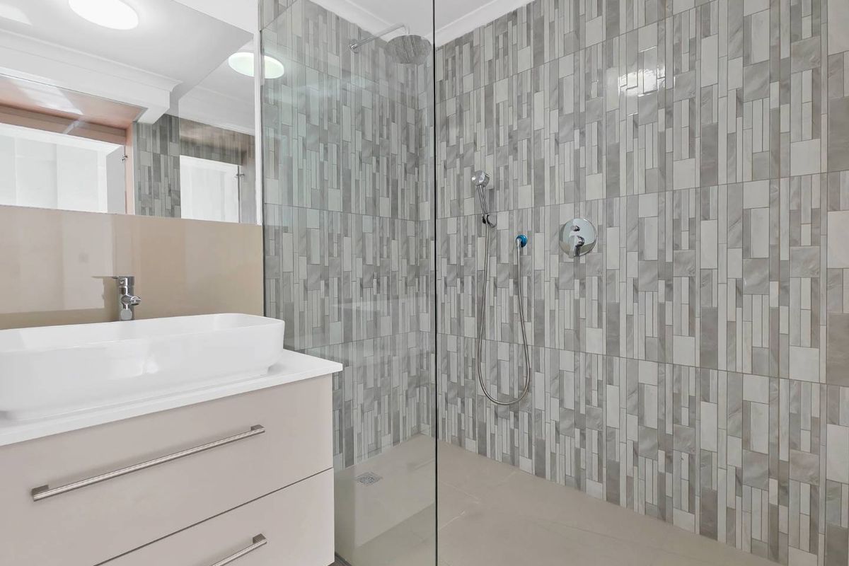 Modern bathroom featuring a sleek vanity with vessel sink, large wall mirror, and a spacious walk-in shower with contemporary grey tiled finishes.