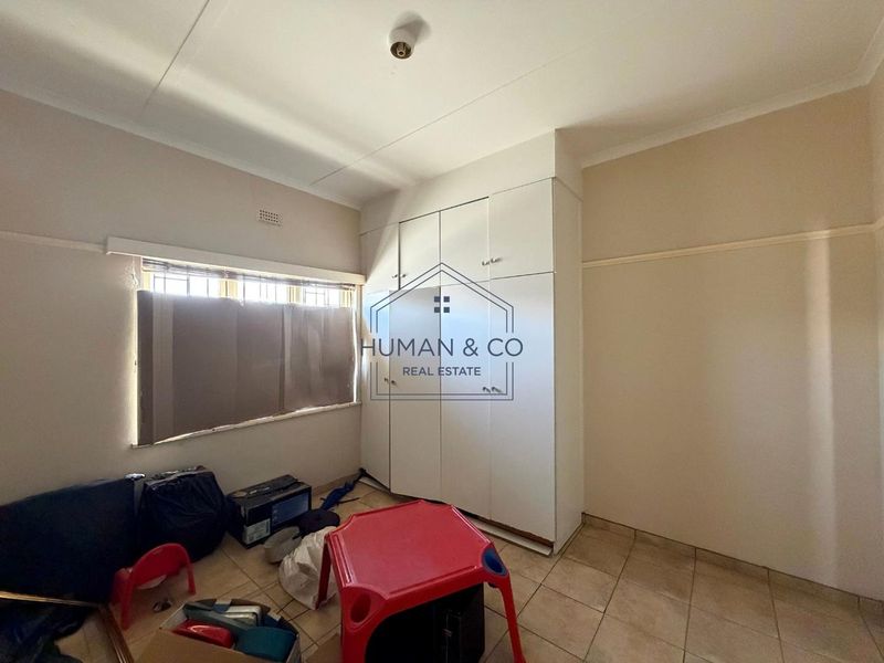 A vacant bedroom featuring built-in cupboards, tiled flooring, and security bars on the window, offering a blank canvas for renovation.