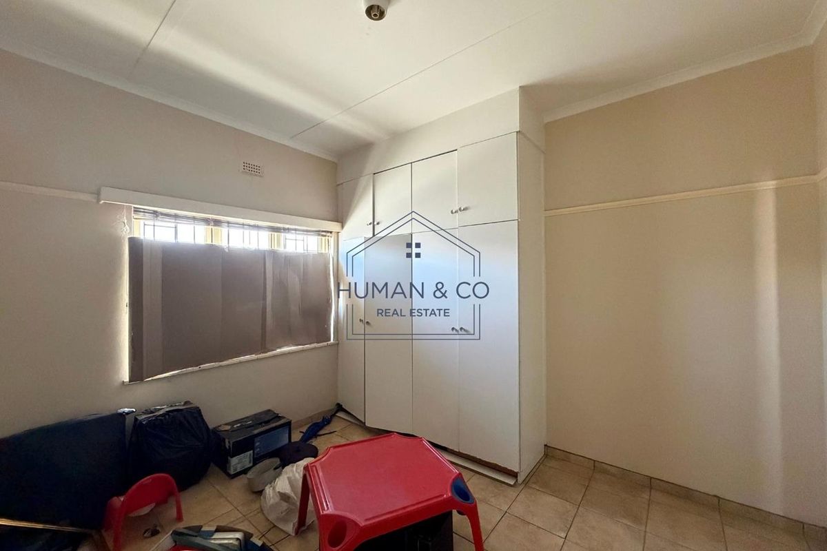 A vacant bedroom featuring built-in cupboards, tiled flooring, and security bars on the window, offering a blank canvas for renovation.