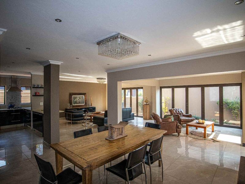 Spacious open-plan living area featuring polished tile floors, modern recessed lighting, crystal chandeliers, and large bi-fold doors leading to the outdoor space.