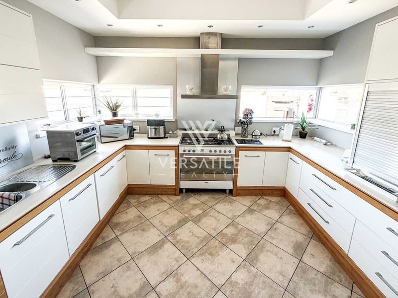 A well-maintained kitchen featuring white cabinetry with wood trim, a gas stove with stainless steel extractor, and tiled flooring.