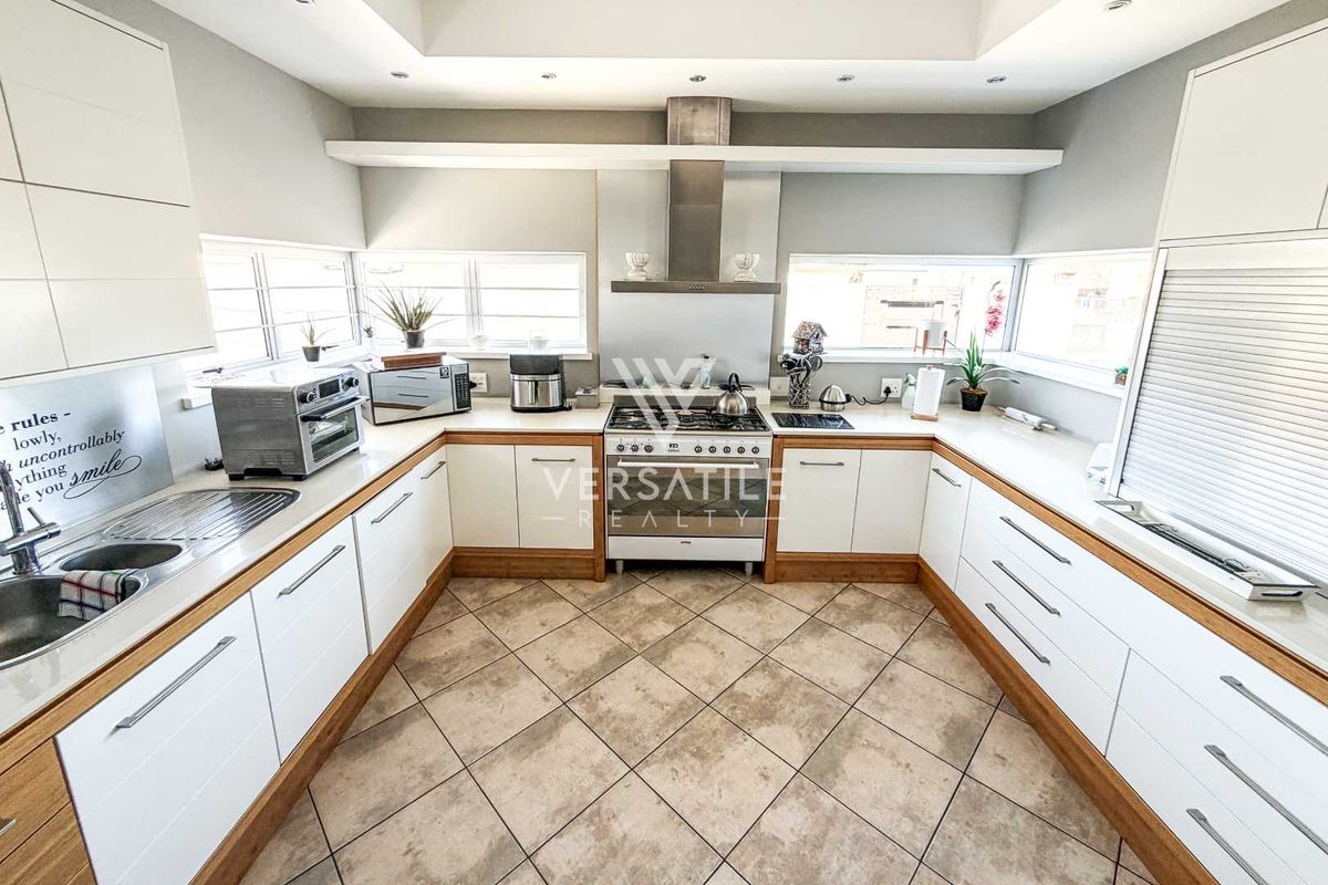 A well-maintained kitchen featuring white cabinetry with wood trim, a gas stove with stainless steel extractor, and tiled flooring.