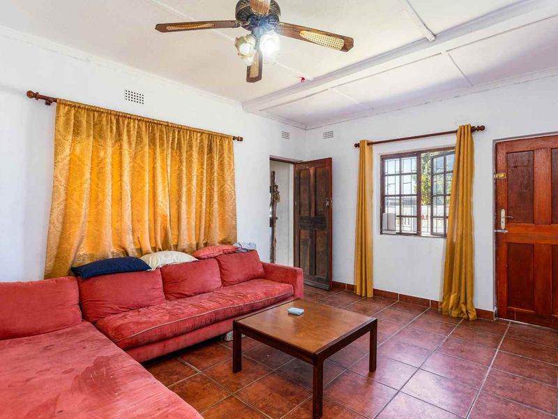 A living room featuring tiled flooring, a ceiling fan, and timber door access, requiring cosmetic updates to improve its overall condition and appeal.