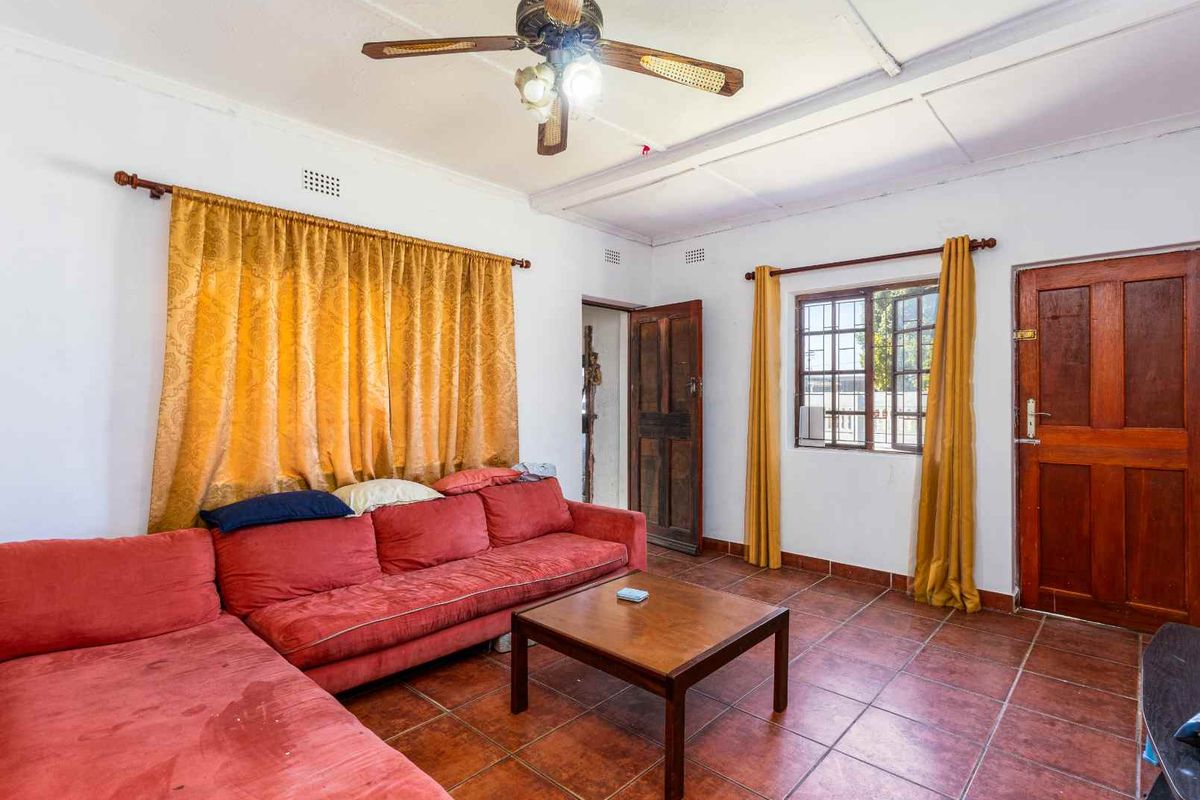 A living room featuring tiled flooring, a ceiling fan, and timber door access, requiring cosmetic updates to improve its overall condition and appeal.