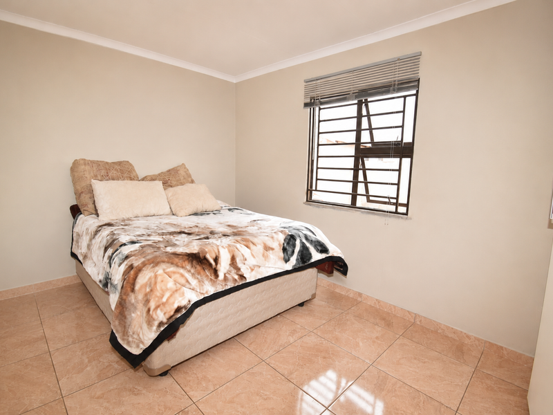 A functional bedroom featuring tiled flooring, a window with security bars and venetian blinds, and a built-in wardrobe.
